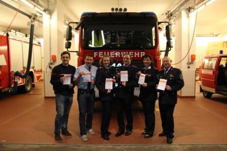 Feuerwehrleute mit Urkunden vorm Feuerwehrfahrzeug